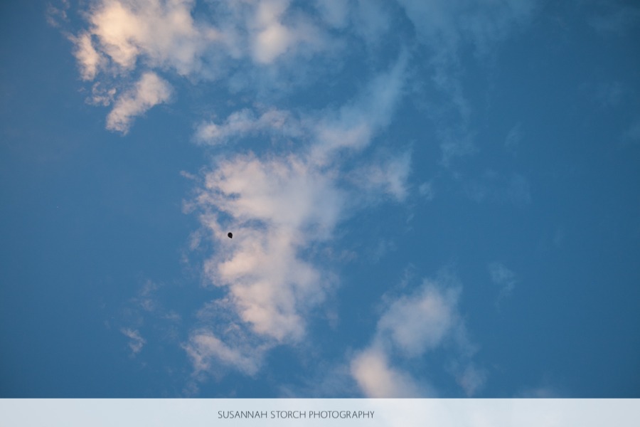 a small balloon floats away into a blue sky with clouds