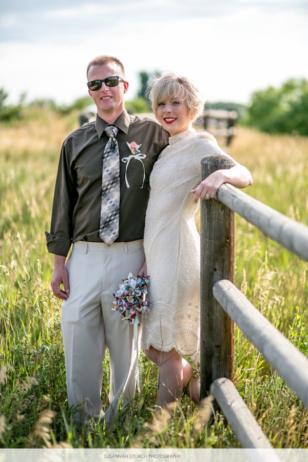 a stylish blonde haired bride and her new husband stands by a fence