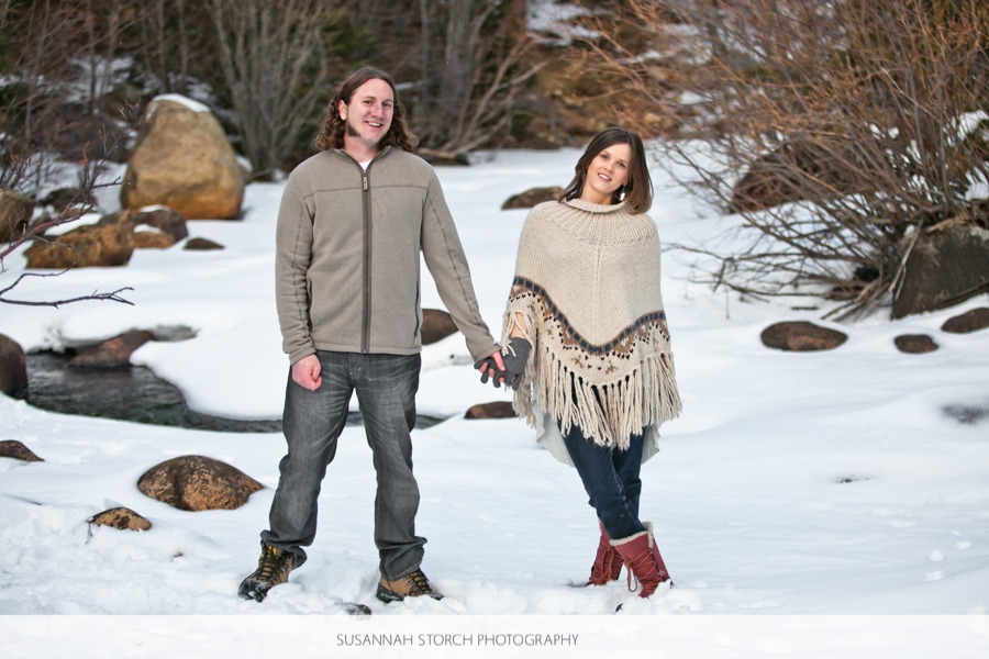 a man and woman stand on top of snow in front of a river