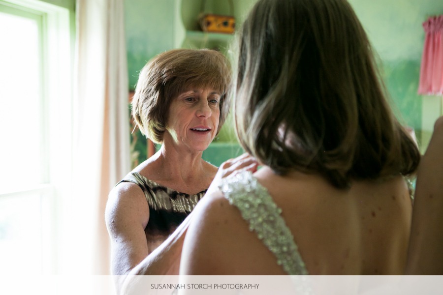 the mother of a bride helps the bride put on jewelry in a green room