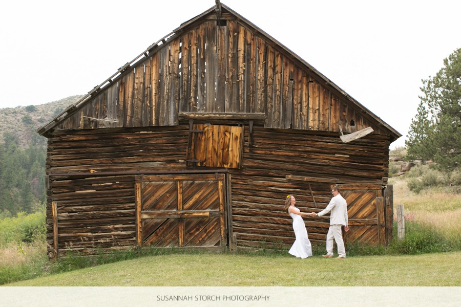 a bride and groom lean away from each other while standing in front of an old wooden barn