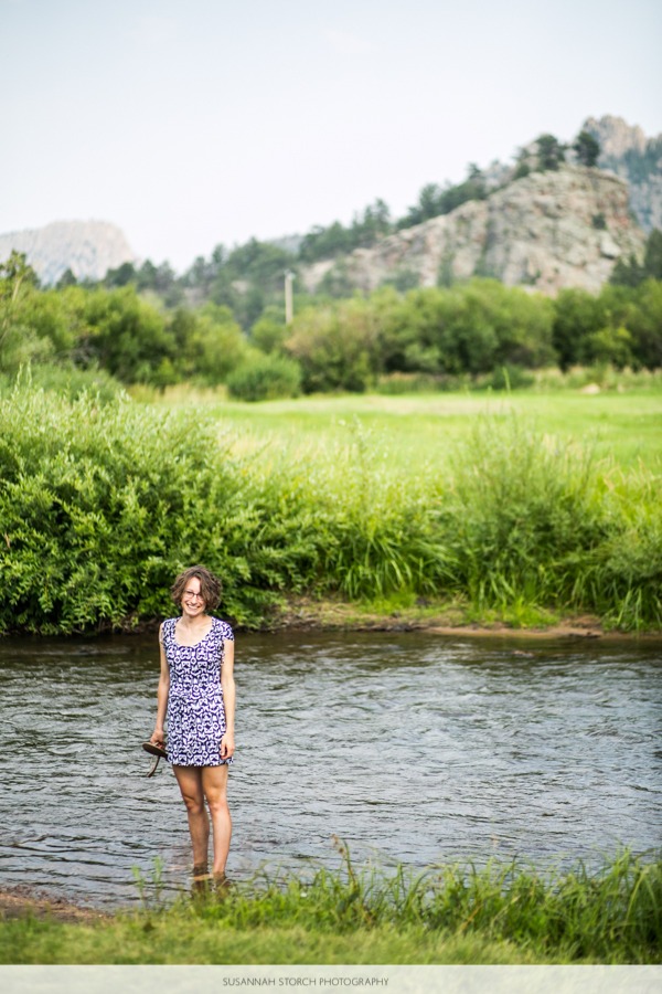 a woman in a dress stands in a small mountain river