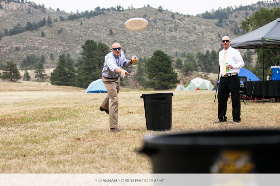 a man throws a frisbee towards a trash can on a dry lawn