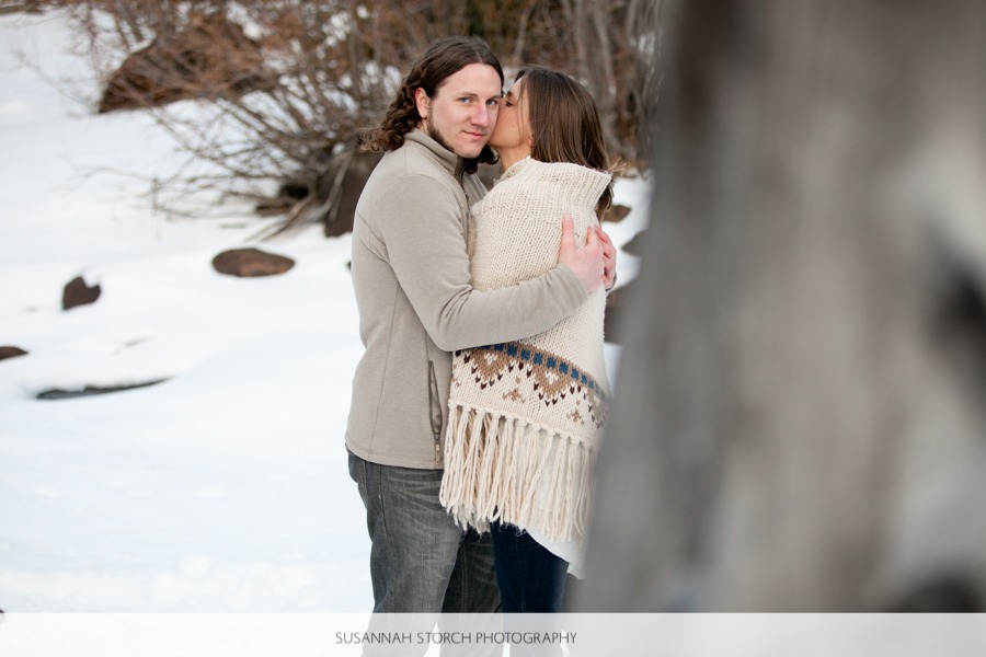 a woman in a poncho kisses a man on the cheek as they stand in the snow