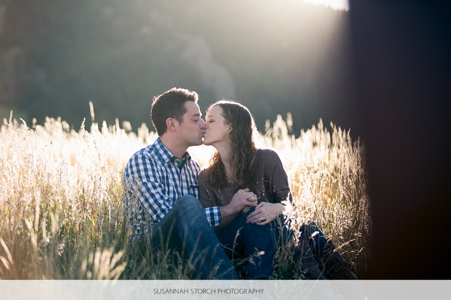 a seated couple kiss in the sunlight in tall grass