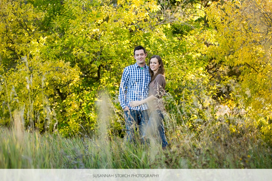 an engaged couple stand together by yellow leaves in trees
