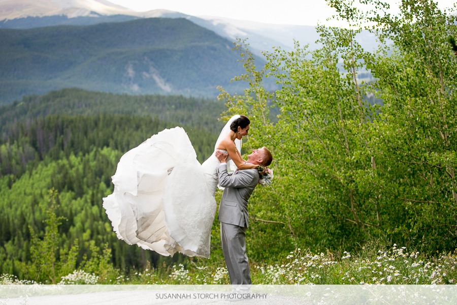 a man lifts a bride up in the air in front of mountains