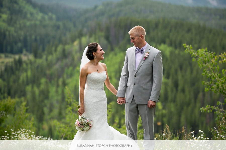 a bride and groom stand in front of green pine trees
