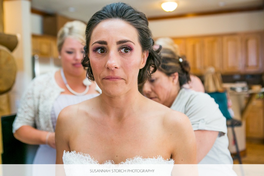 a bride looks teary-eyed as she gets into her wedding dress