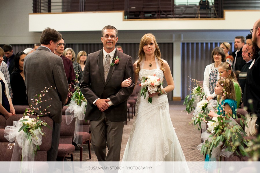 a father walks his daughter, the bride, down a church aisle