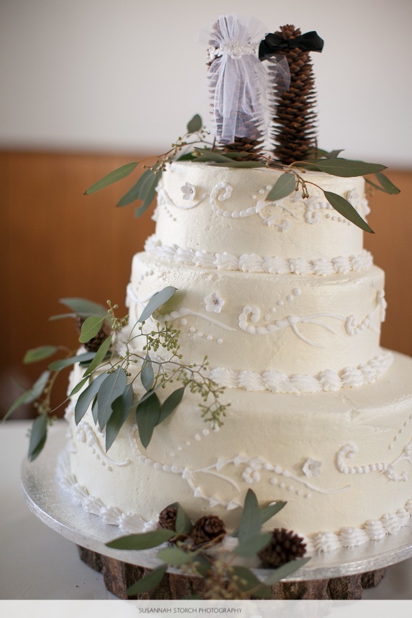 white wedding cake on a wooden log with leaves and pinecones