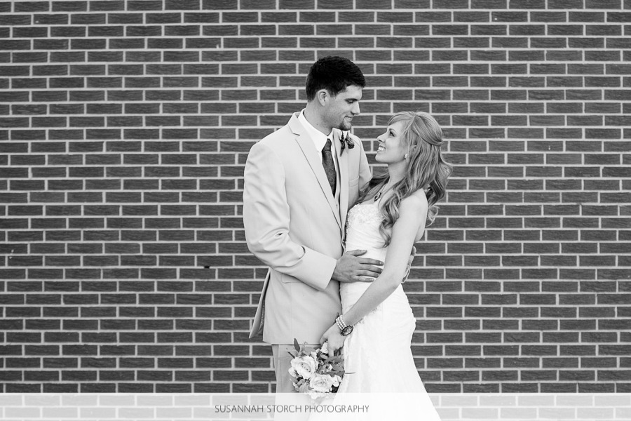 black and white photo of a bride and groom looking at each other in front of a brick wall