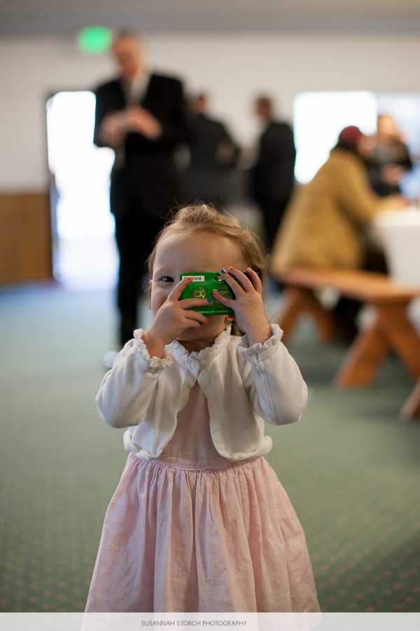 a young girl in a pink dress holds a disposable camera up to her face