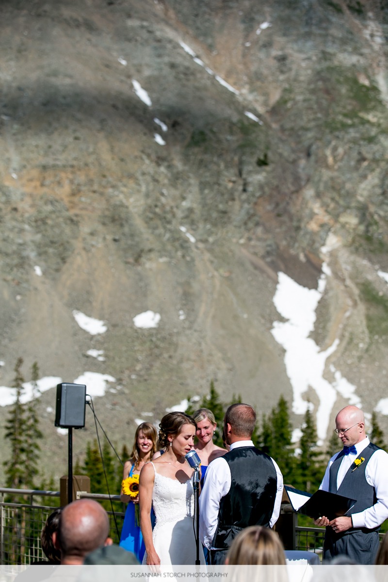 a bride speaks into a microphone in front of rugged mountains
