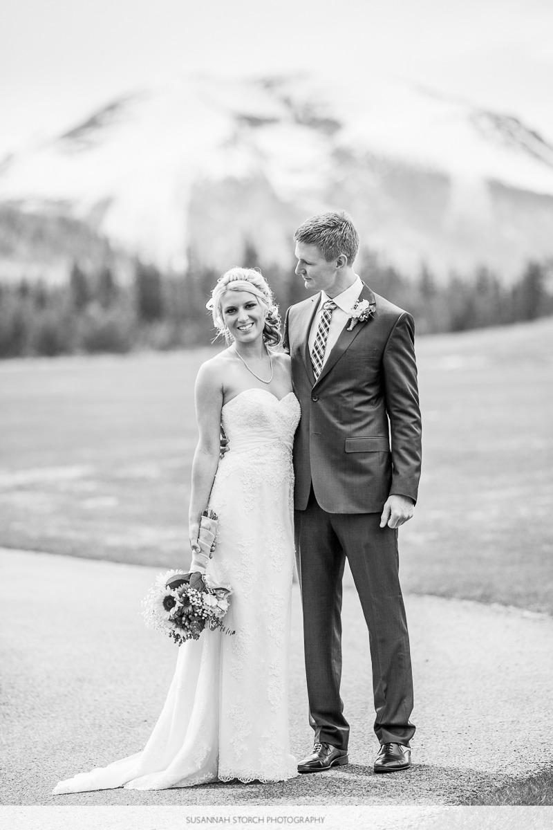 black and white photo of a bride looking at the camera while her groom looks at her