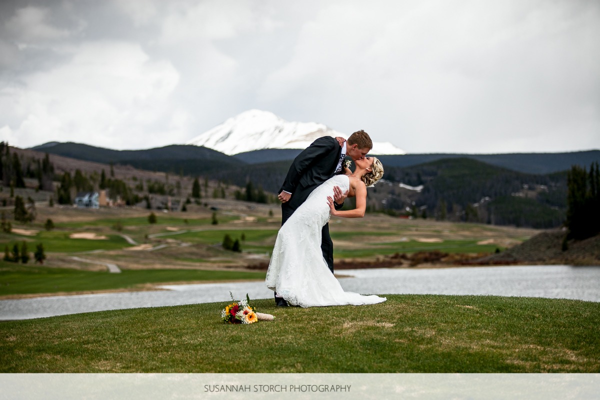 a groom dips his bride and kisses her on a mountain golf course