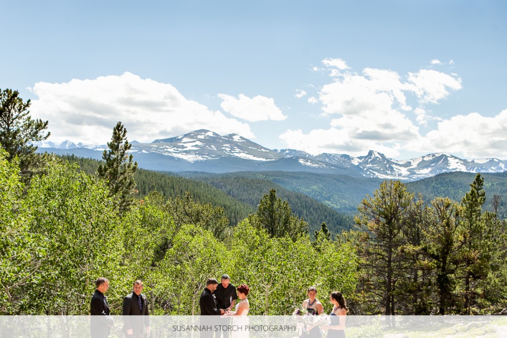 wide angle image of a wedding ceremony taking place under blue skies and in front of rugged mountains