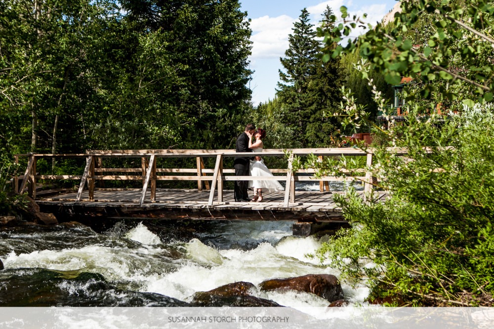 a man and woman kiss on a wooden bridge over a rocky river