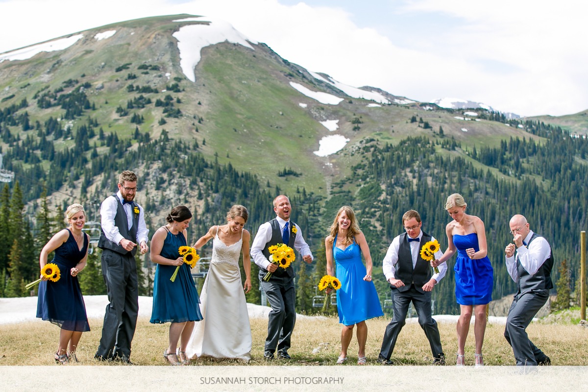 a wedding party dances in front of a snow-capped mountain