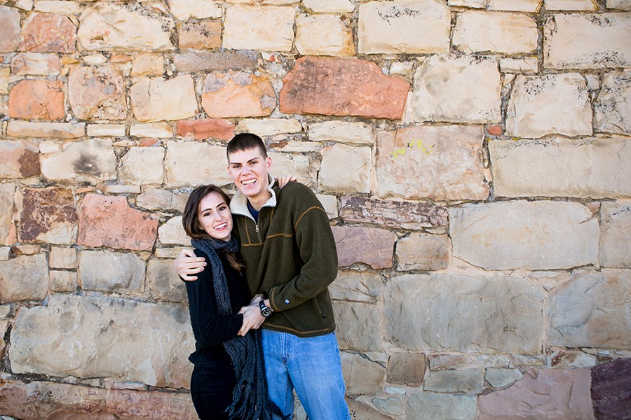 a brother and sister stand in front of a rock wall
