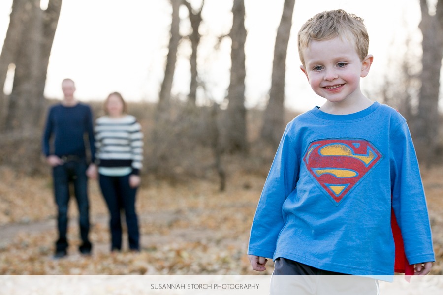a toddler dressed as superman stands in front of his parents