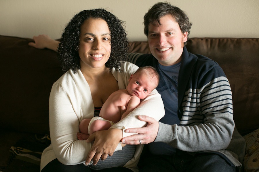 parents sit on a couch while holding their baby boy