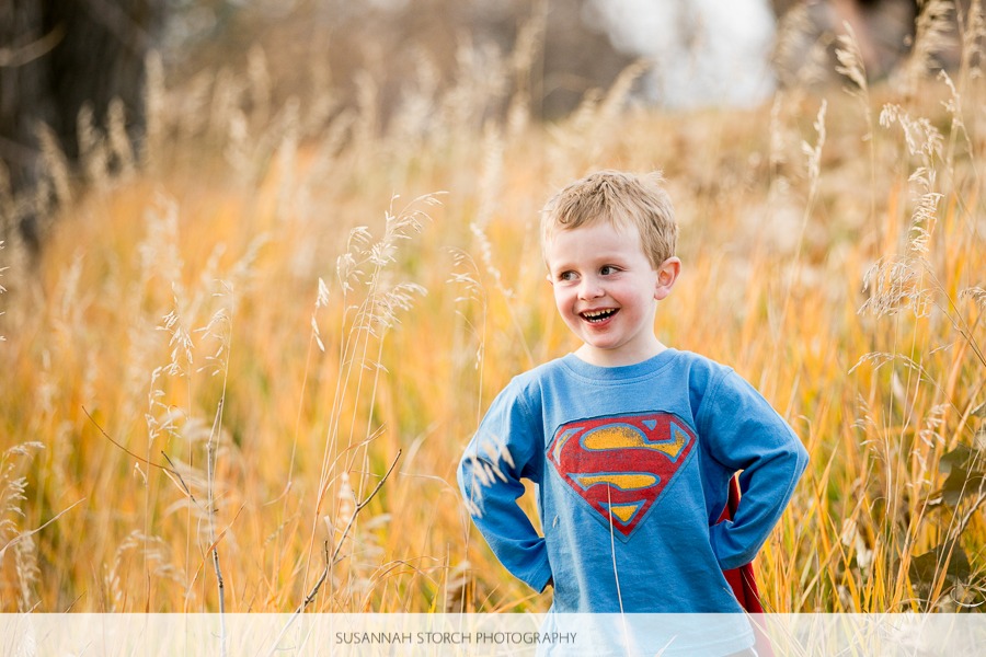 a toddler boy smile sin front of fall color while wearing a superman tee