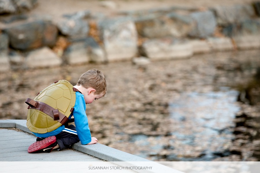 a boy wearing a turtle shell looks out at a pond
