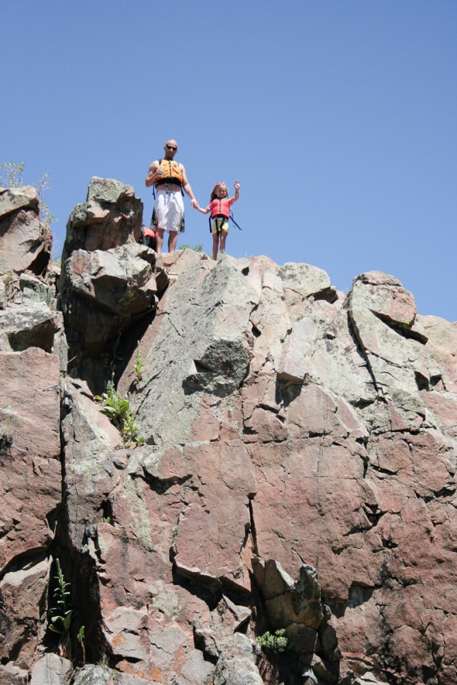 a man and young girl hold hands at the top of a steep rock formation
