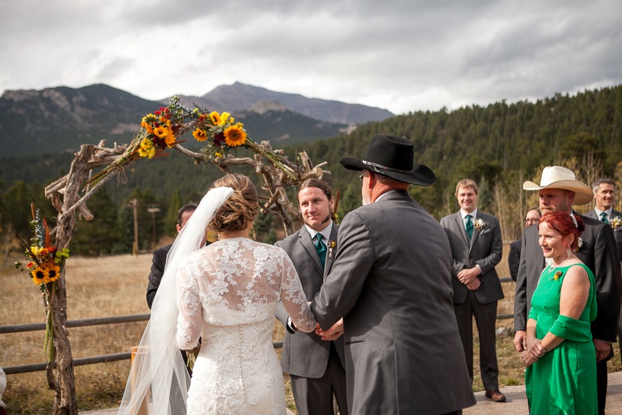 a father in a black cowboy hat is about to hand off his daughter to the waiting groom