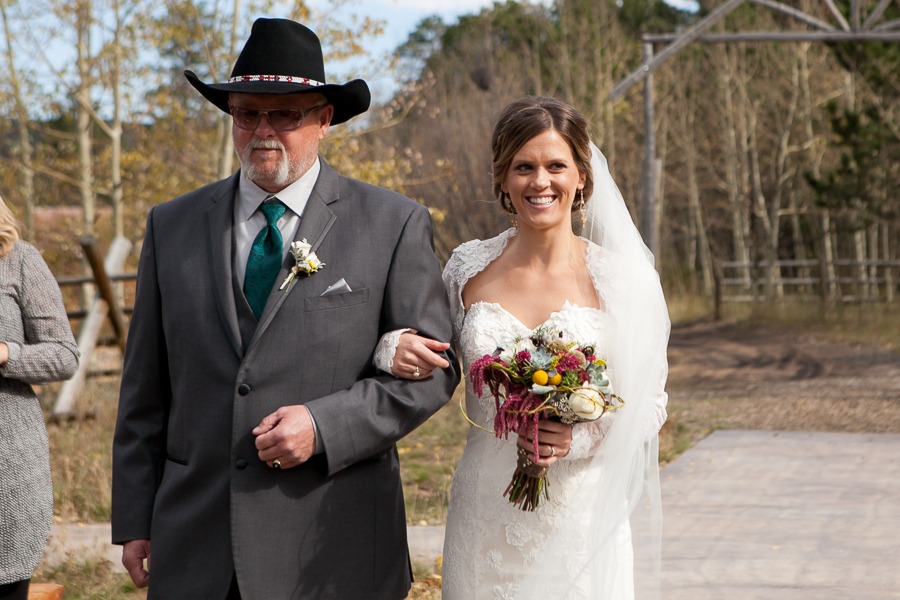 a father in a hat walks his daughter down the aisle at an outdoor wedding