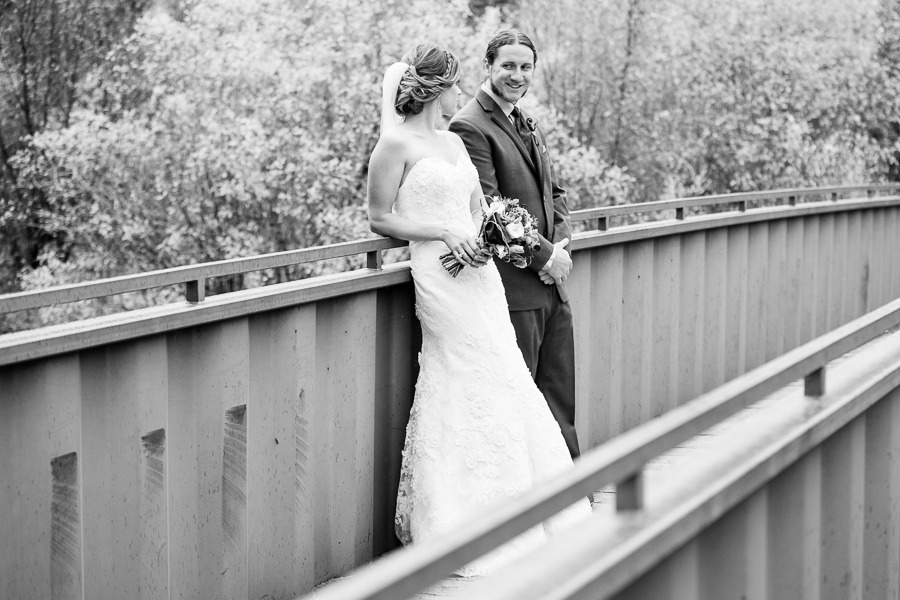 a groom smiles at his wife as they stand on a bridge