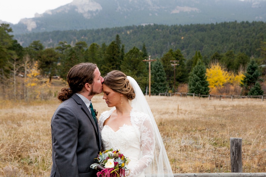 a groom kisses the forehead of a bride in the mountains