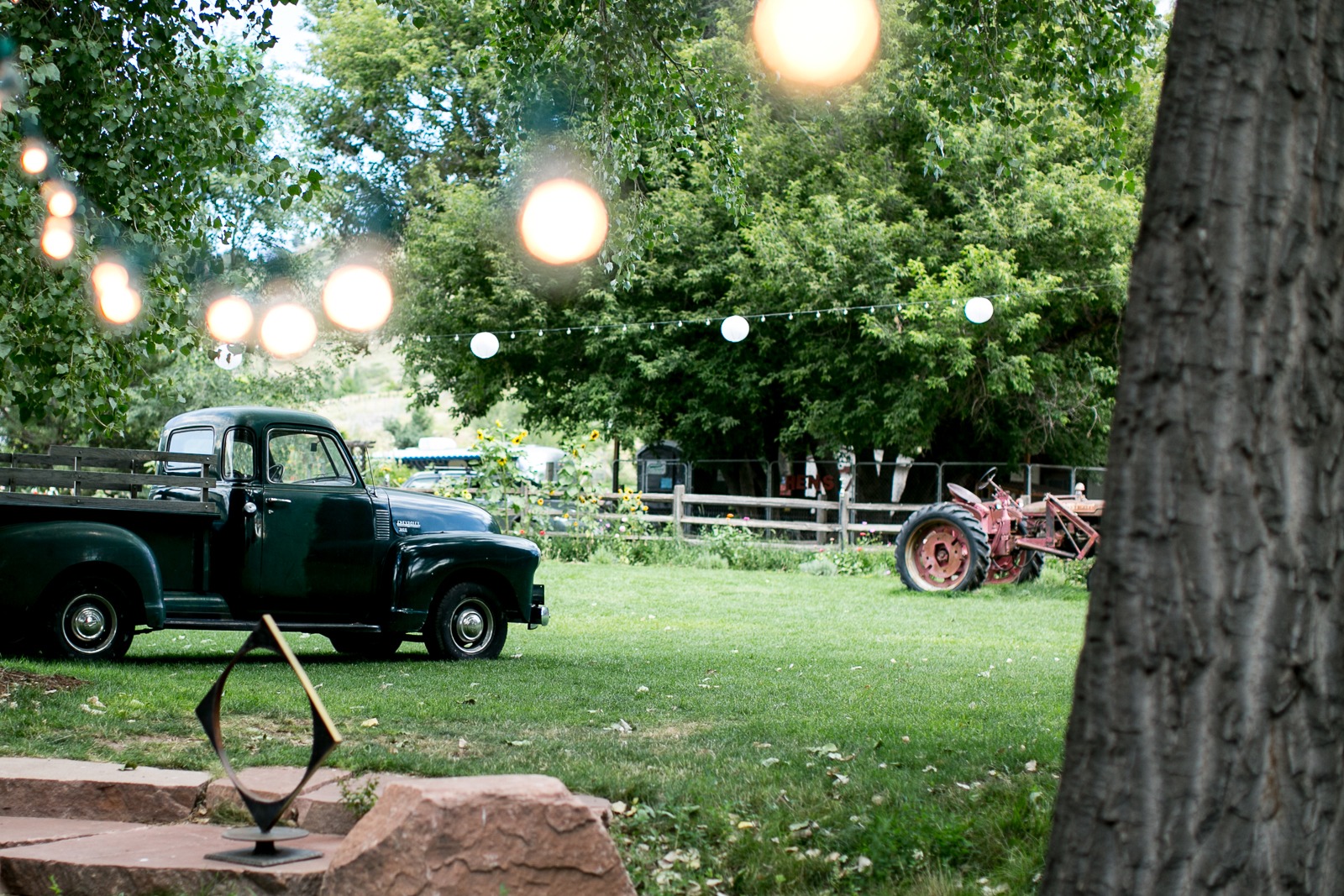 an old truck and tractor sit ona lawn under fairy lights