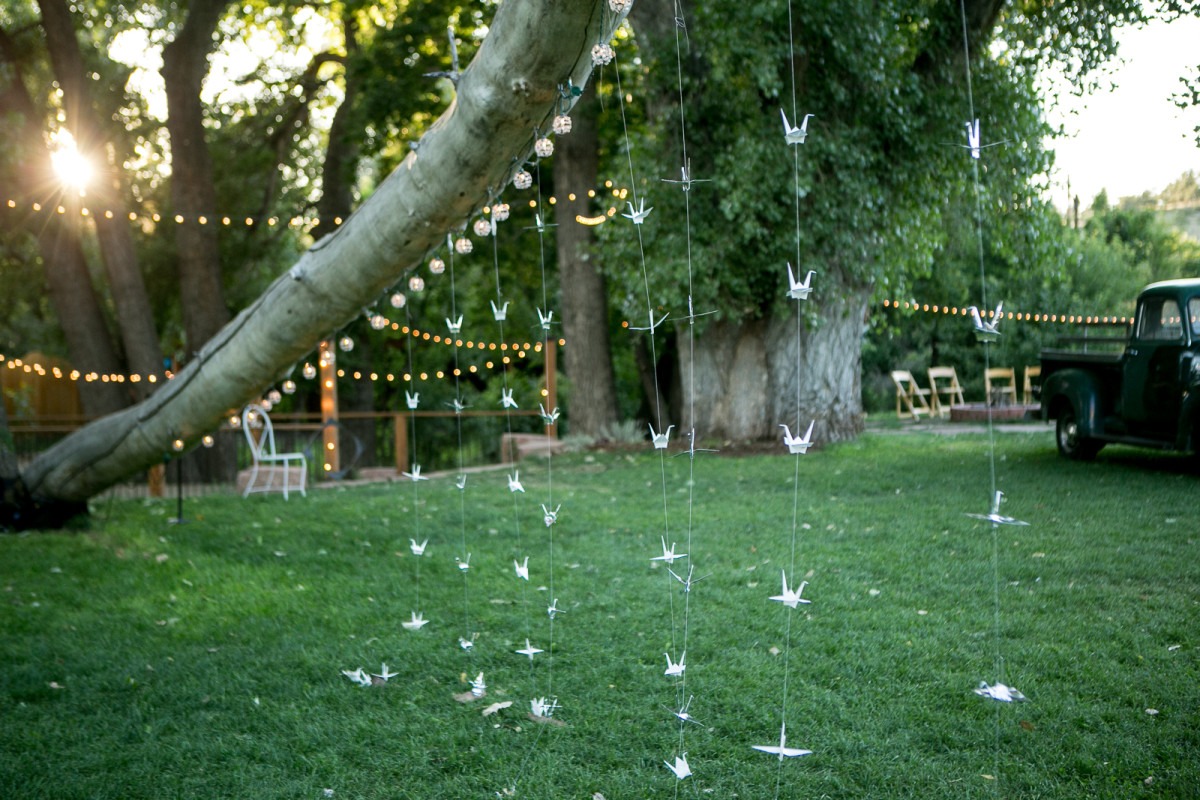 white paper cranes hang from a tree trunk while sun shines through the trees