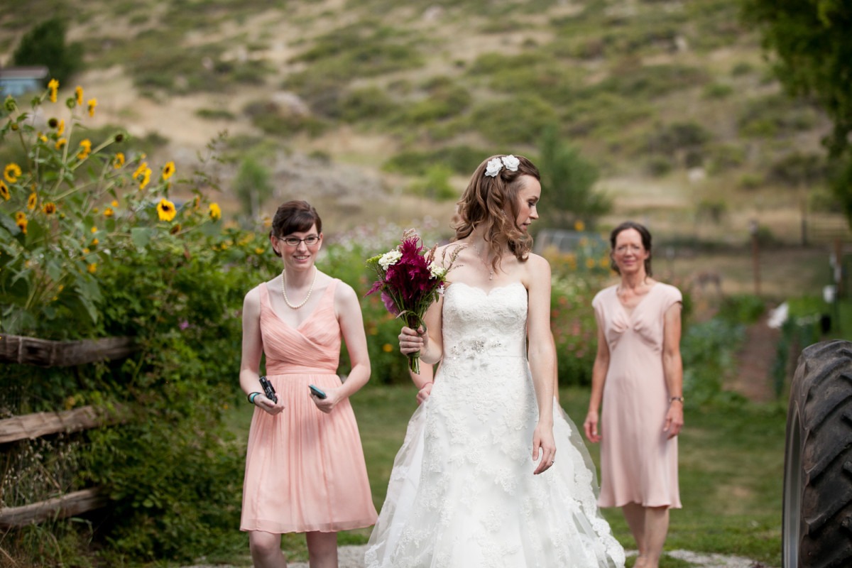 a bride looks back as she walks in front of a bridesmaid in pink and her mother in pink