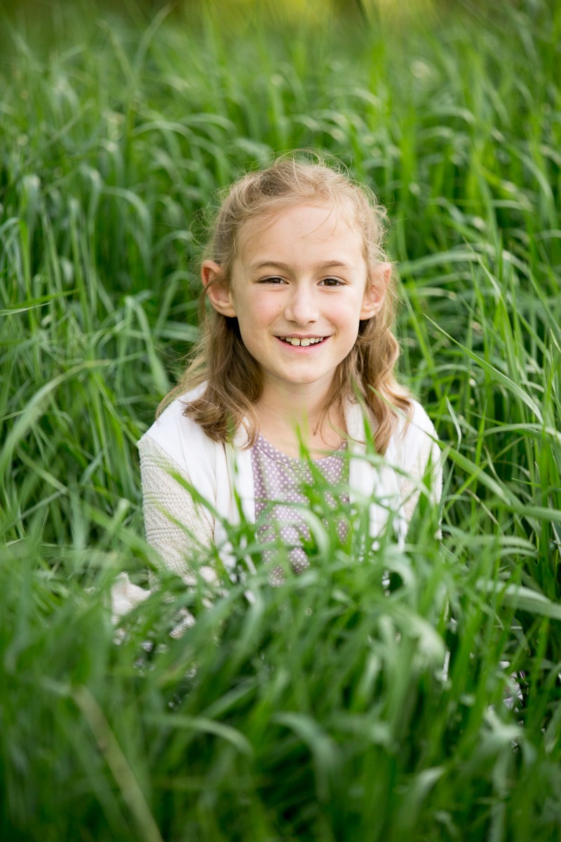 a girl sits in tall green grass