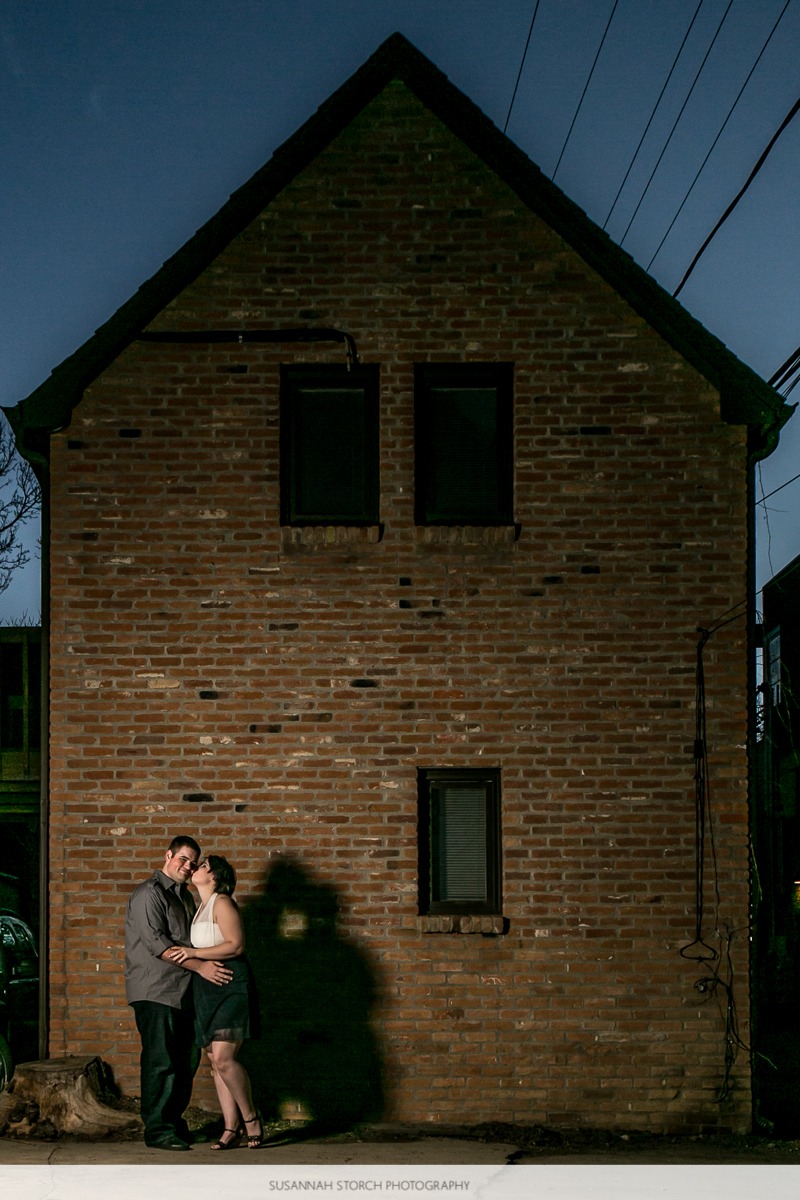 a woman kisses a man in front of a small brick building at night