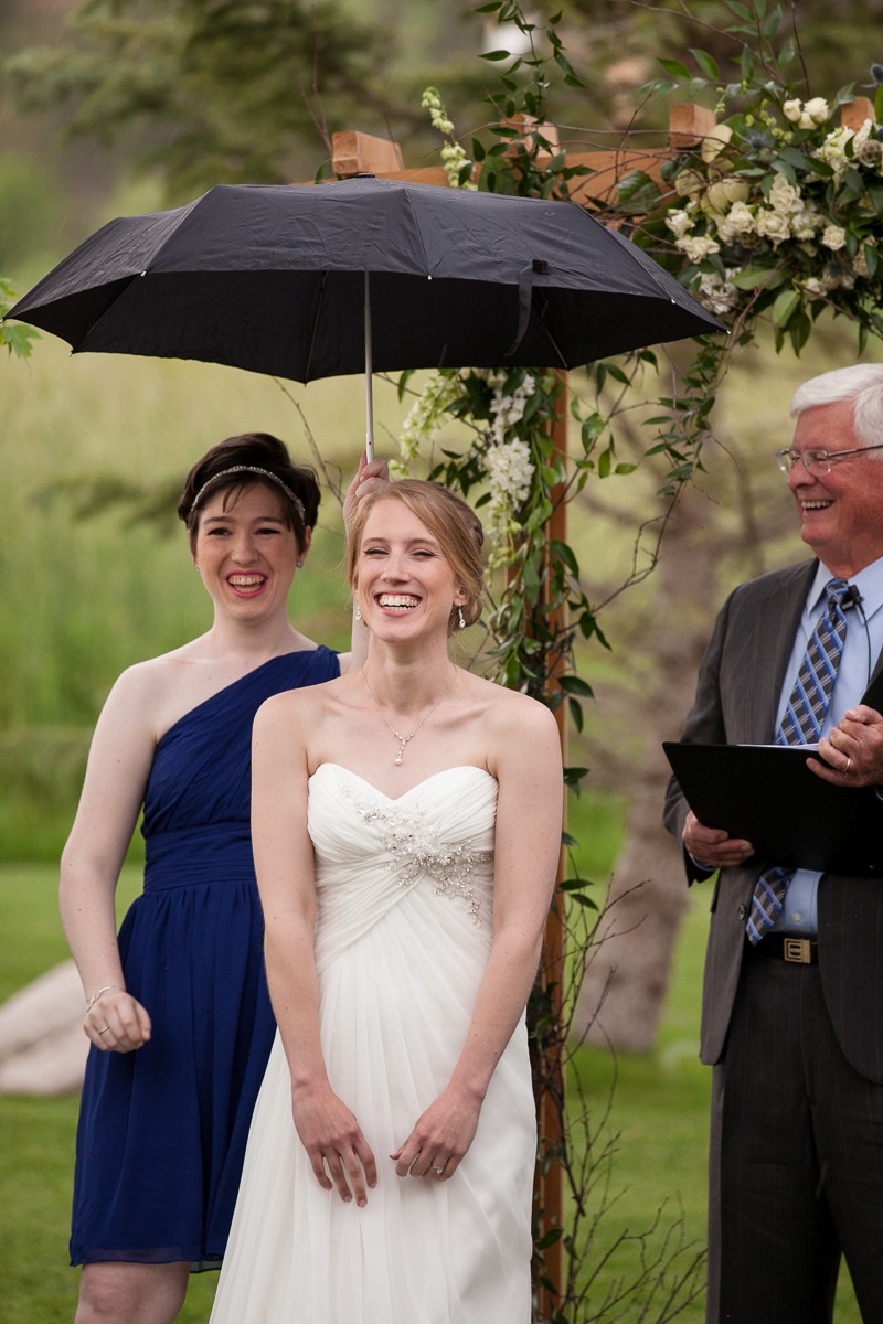 a bride laughs during her outdoor wedding ceremony while standing under an umbrella