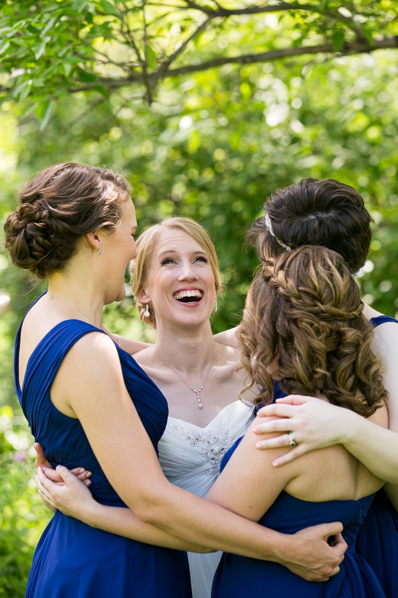 a smiling bride looks up into the sky while being hugged by bridesmaids