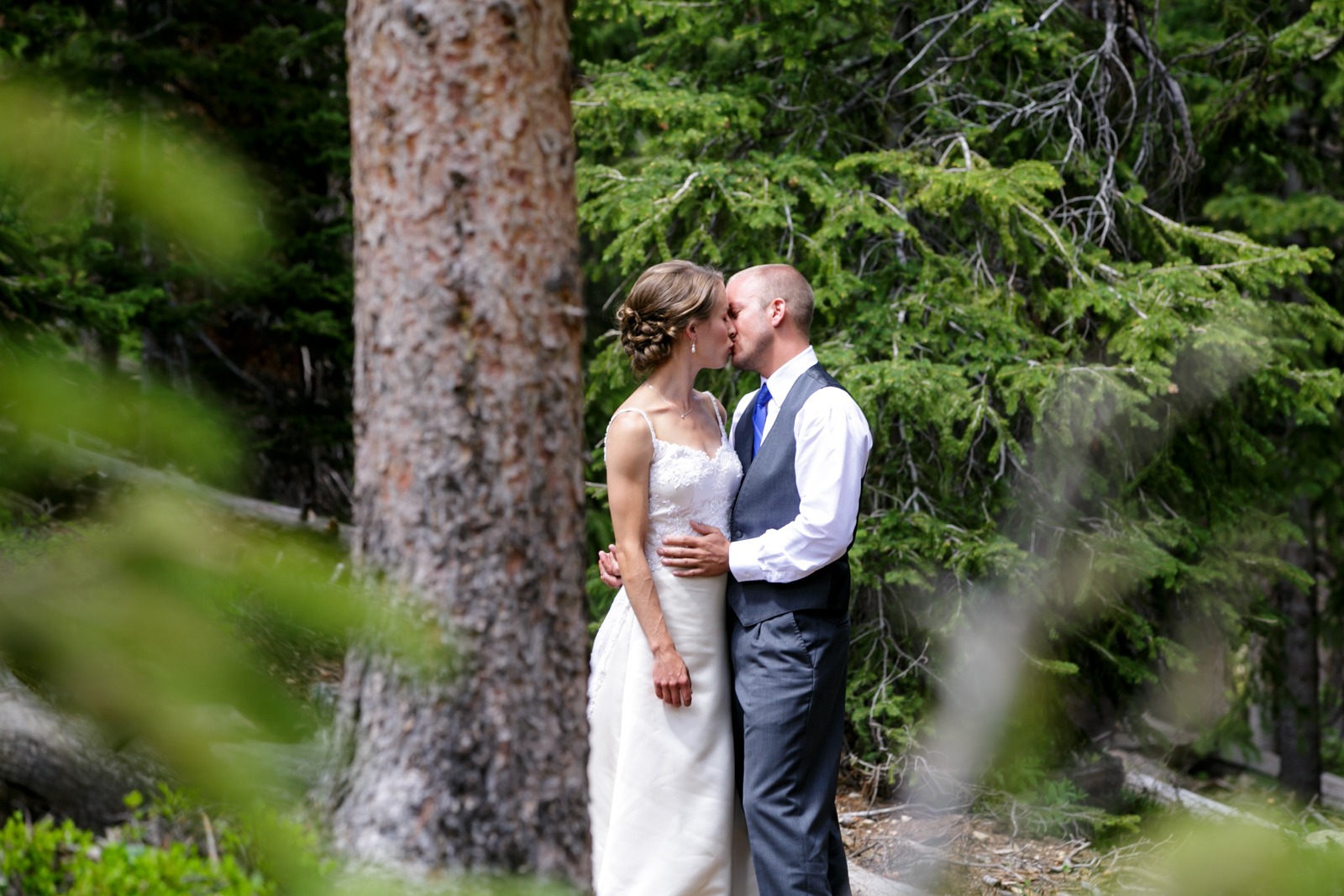 a bride and groom kiss by an old tree trunk