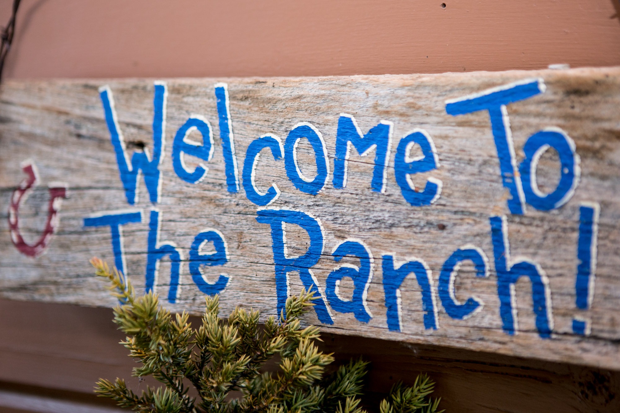 wooden sign painted with blue words that say welcome to the ranch