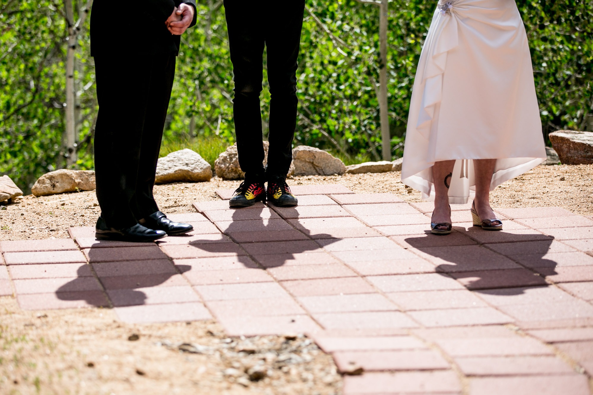 the legs of two men and one women with their shadows projecting on pavers