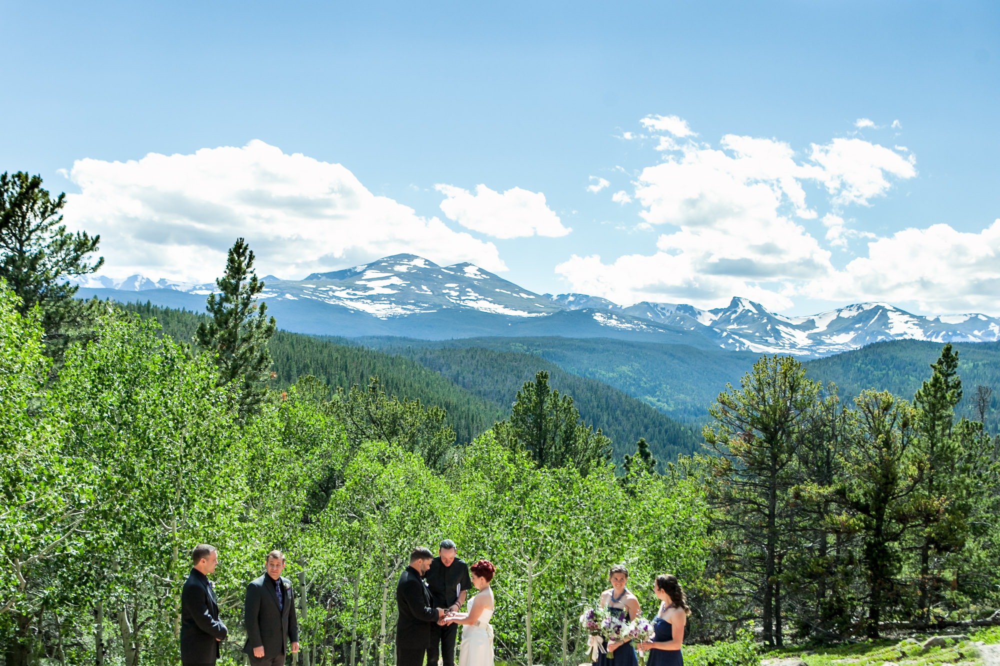 a wedding ceremony takes place in front of snow-capped mountains and blue skies with white clouds