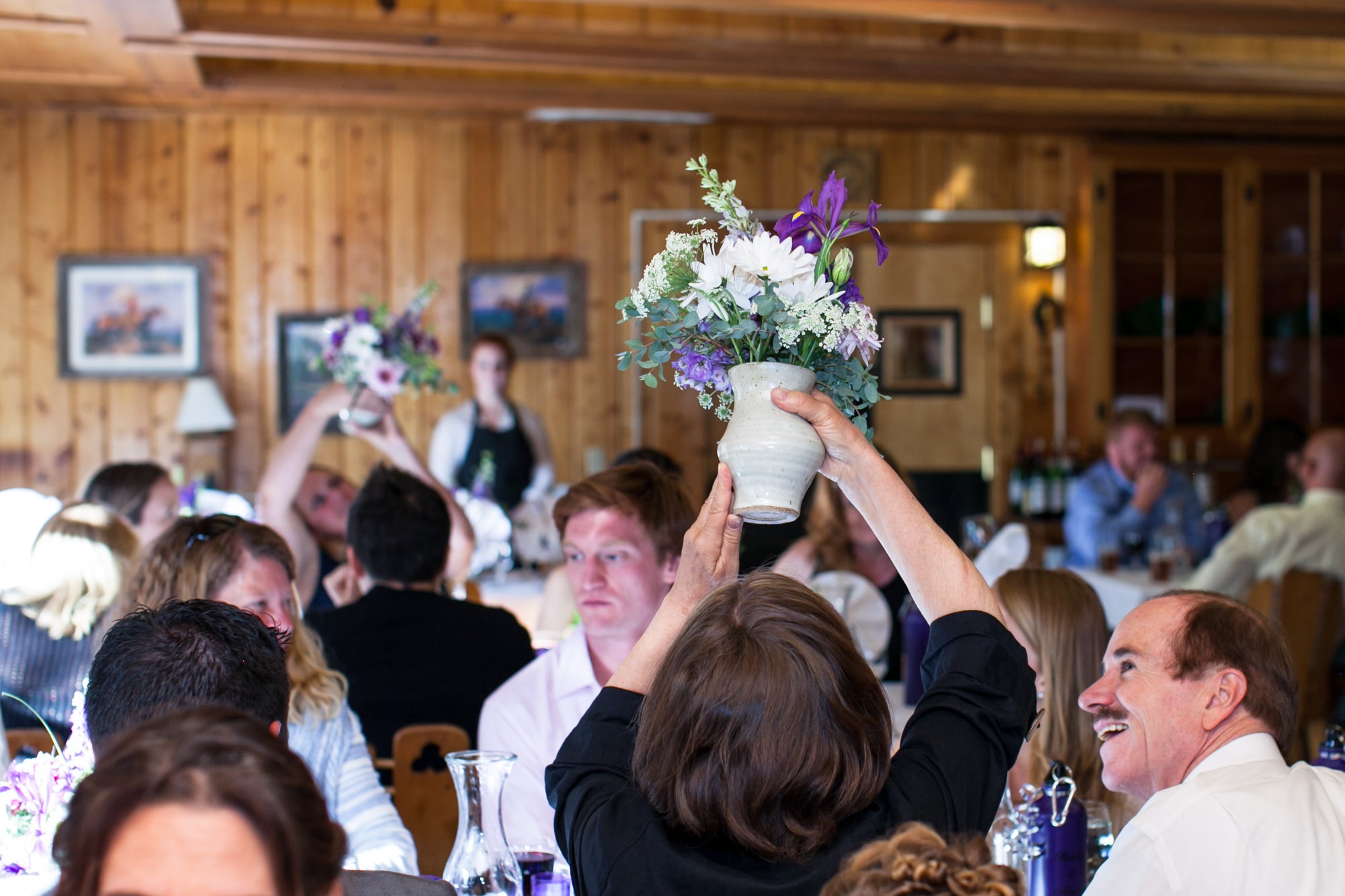 a woman sitting at a wedding table picks up a vase of flowers and looks at the bottom of the vase