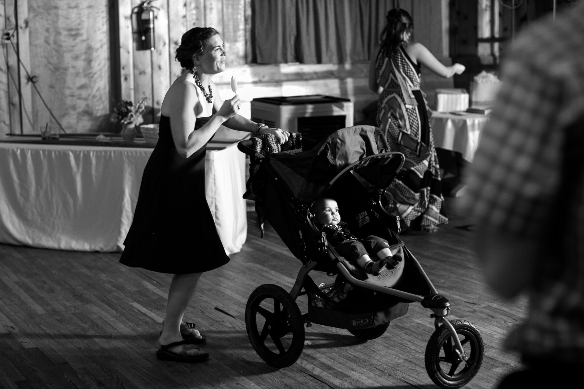 black and white image of a woman eating a popsicle while standing behind a baby stroller with a relaxed baby