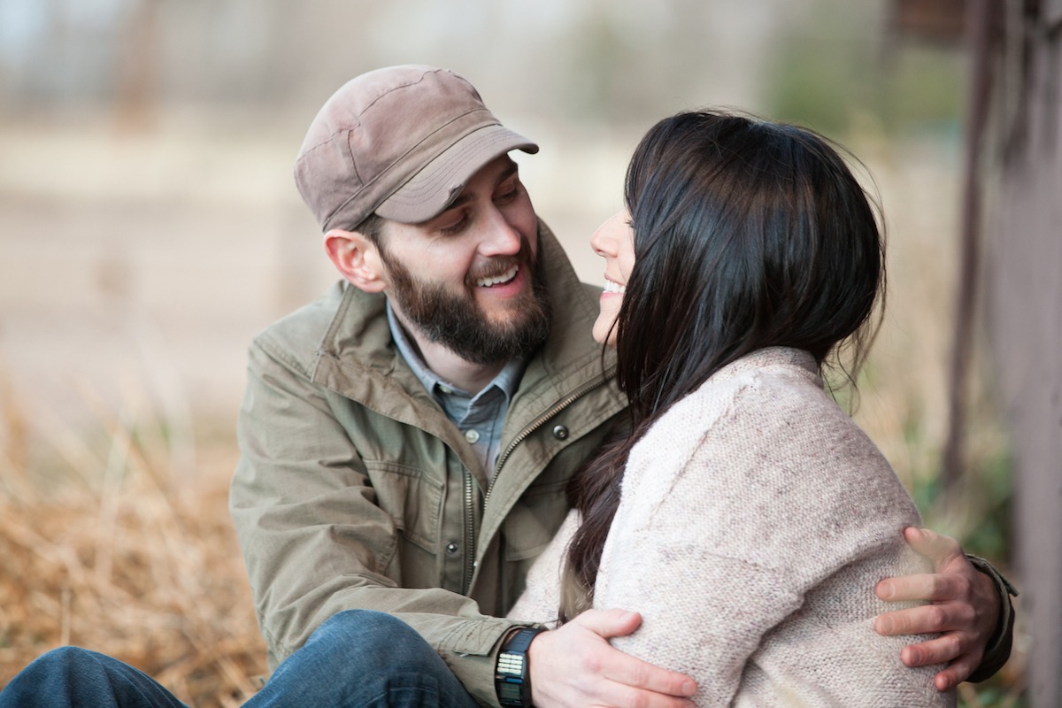 a man with hat and beard wraps his hands around his brunette fiancee