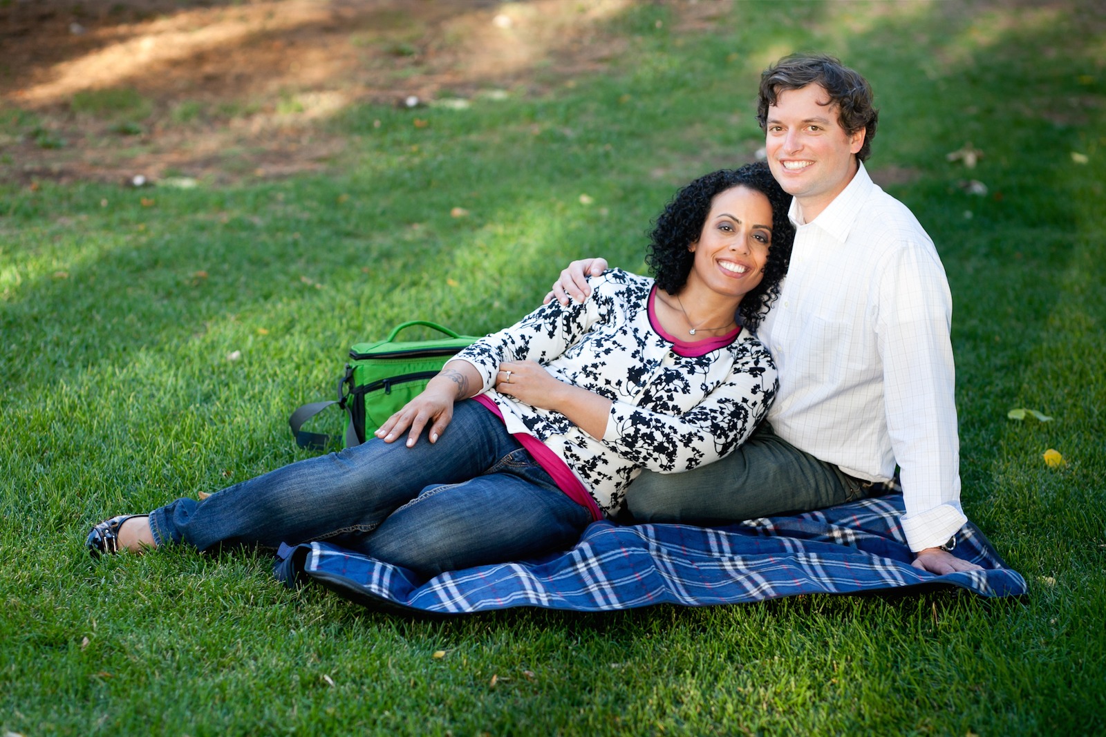 a woman leans against a man as they both sit on a blue picnic blanket