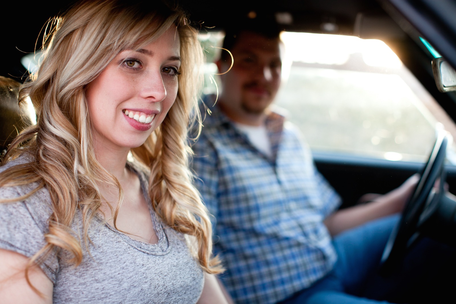 a blonde woman sits in the passenger seat of a car and looks at the camera