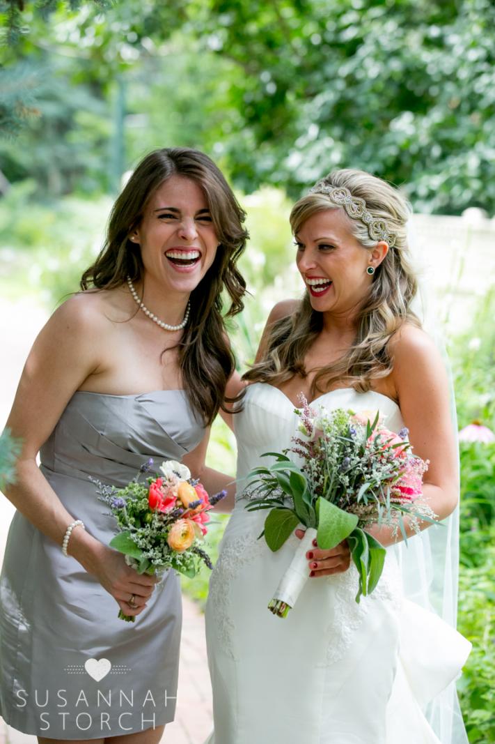 a bridesmaid and the bride laugh while holding colorful bouquets